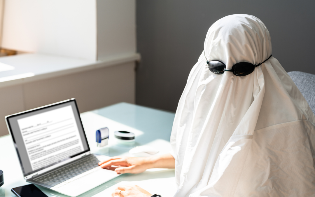 Person dressed as a ghost sitting at a desk with estate planning documents on a laptop, representing an outdated estate plan that no longer reflects current wishes or circumstances.